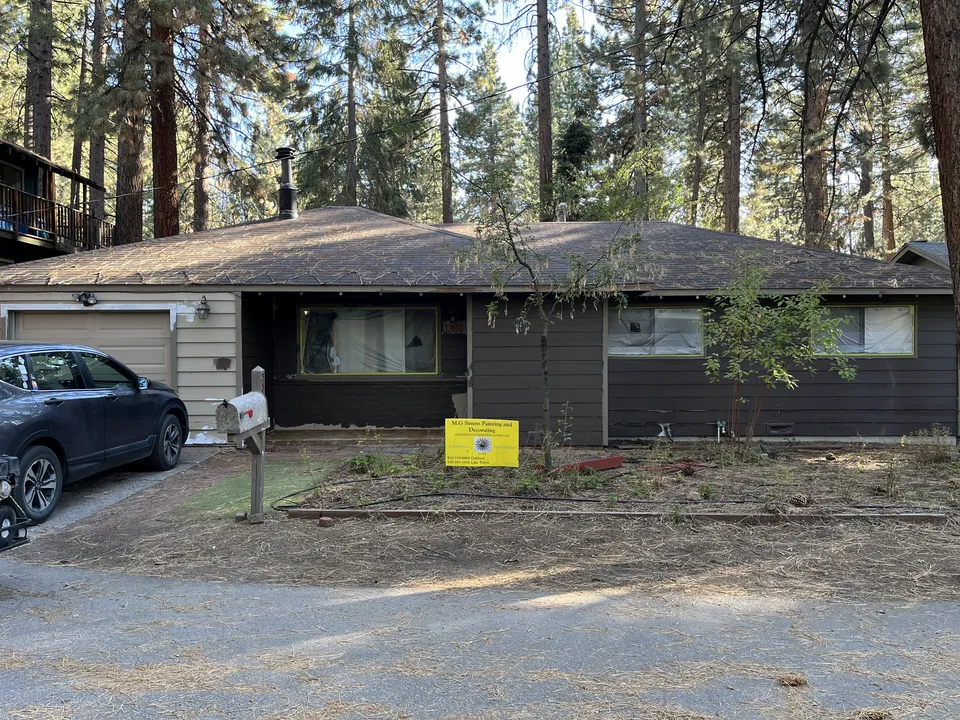 Ranch-style home surrounded by pine trees after a full exterior painting.