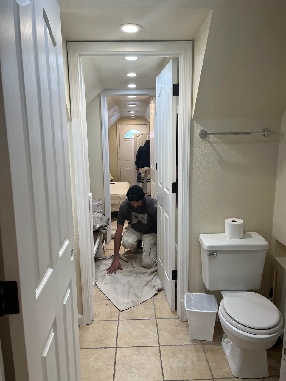 Painter working in an interior hallway next to a bathroom doorway.